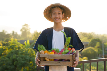 Happy asia farmer smiling while carrying full basket of vegetable at organic farm.