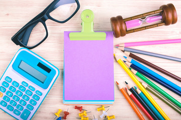 Top view office desk with mock up pencils, calculator, hourglass and blank notepad for text