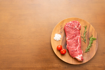 Fresh raw beef sirloin steak with cherry tomato, rosemary and salt on wood plate, Wood background, Copy space on the left