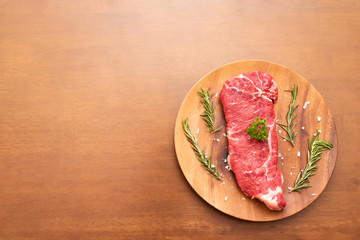 Fresh raw beef sirloin steak with parsley, rosemary and salt on wood plate, Wood background, Copy space on the left