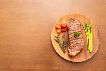 Fresh cooked sirloin beef steak with rosemary, tomato, asparagus and top with parsley on wood plate, Wood background, Copy space on the left