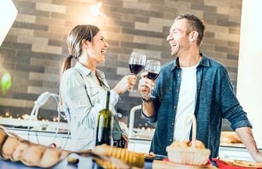 Young couple in love drinking red wine at house kitchen - Happy millenial people at home enjoying...