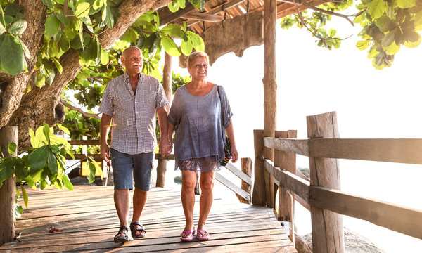 Happy senior couple walking holding hand at Koh Phangan beach promenade - Active elderly and travel lifestyle concept with retired mature people at Thailand luxury resort - Bright warm day filter