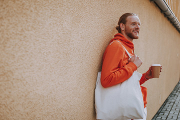 Red haired man leaning on wall with coffee