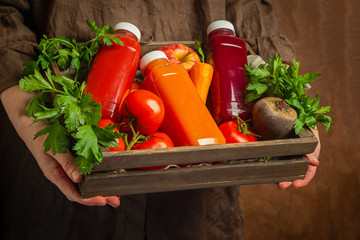 Fresh juice smoothies from various vegetables carrot apple beet tomatoes in bottles in a wooden box in female hands.