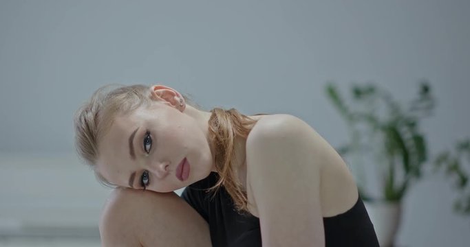 Pretty young woman with her hair in a ponytail opening her eyes before resting her head on her knees watching the camera. RAW video record.