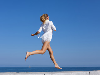 Fototapeta premium Barefoot girl in white short dress running along breakwater