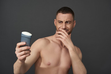 Fototapeta premium Waist up of Caucasian guy holding male cosmetics for armpits in arm