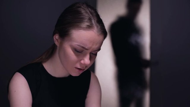 Frightened woman crying, tyrant husband entering room, domestic violence victim