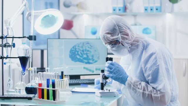 Chemist scientist looking into microscope in modern high end laboratory with 3D scans of brain and DNA on the displays