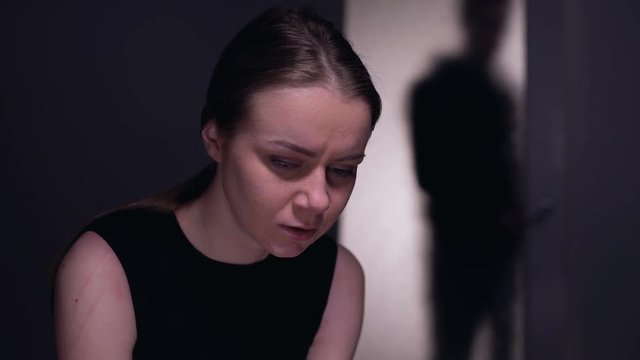 Scared kidnapping victim looking at male silhouette entering room, mistreatment
