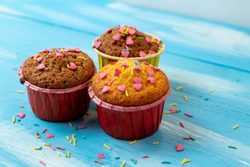 Delicious homemade colorful cupcakes with heart-shaped confectionery close up on a light blue wooden background