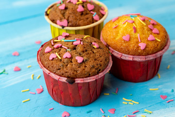 Delicious homemade colorful cupcakes with heart-shaped confectionery close up on a light blue wooden background