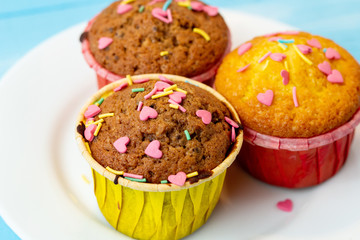 Delicious homemade colorful cupcakes with heart-shaped confectionery close up on a light blue wooden background