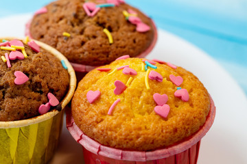 Delicious homemade colorful cupcakes with heart-shaped confectionery close up on a light blue wooden background