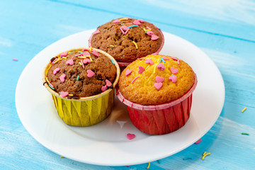 Delicious homemade colorful cupcakes with heart-shaped confectionery close up on a light blue wooden background