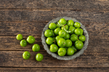 Many isolated green sour plums in a bowl on the rustic wooden table