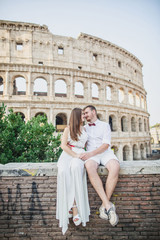 Fototapeta na wymiar young beautiful couple in white clothes stands against the background of the Colosseum in Rome in Italy