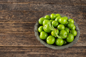 Many isolated green sour plums in a bowl on the rustic wooden table