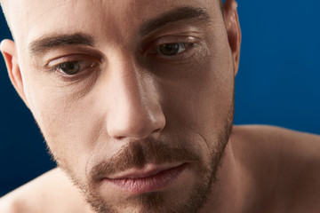 Portrait of upset handsome bearded young man looking down in studio
