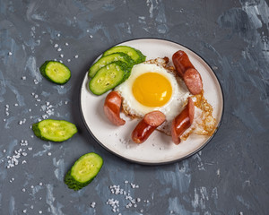 Scrambled eggs and hunting sausages on a round plate for a quick Breakfast of a single bachelor, slices of fresh cucumber