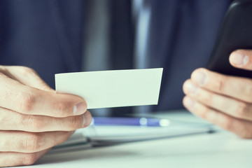Businessman holding blank business card and dialing numbers on mobile phone