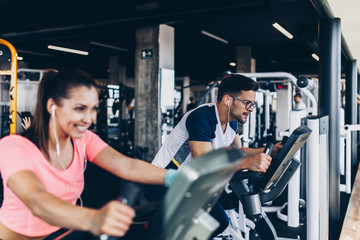 Young and attractive woman and man biking in the fitness gym. They exercising legs and doing cardio...
