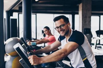 Young and attractive woman and man biking in the fitness gym. They exercising legs and doing cardio...