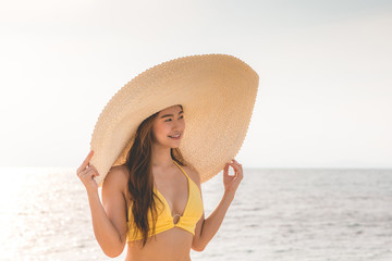 Attractive Asian young woman wearing yellow bikini smile enjoy with summer vacation on the beach feeling so happiness and cheerful,Travel in tropical beach in Thailand,vacations and relaxation Concept