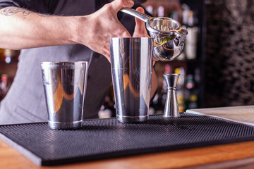 barman in bar interior squeezes lime juice into a chilled shaker. Portrait of a professional bartender at work in night club with squeezer in hands. Service industry occupation.