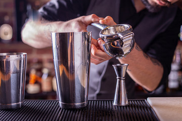 barman in bar interior squeezes lime juice into a chilled shaker. Portrait of a professional bartender at work in night club with squeezer in hands. Service industry occupation.