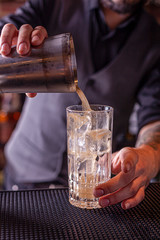 Bartender pouring a cocktail from the steel shaker on the bar counter on the blurred background