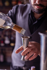 barman preparing cocktai and pours liquid into the jigger in a cocktail bar