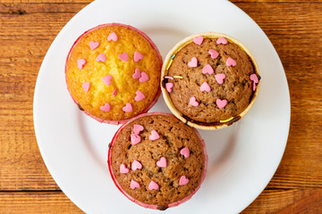 Delicious homemade colorful cupcakes with heart-shaped confectionery close up on a brown wooden background