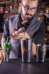 barman preparing cocktai and pours liquid into the jigger in a cocktail bar