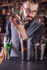 barman preparing cocktai and pours liquid into the jigger in a cocktail bar