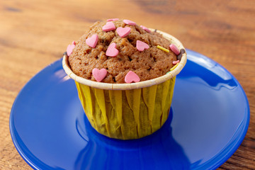 Delicious homemade colorful cupcakes with heart-shaped confectionery close up on a brown wooden background