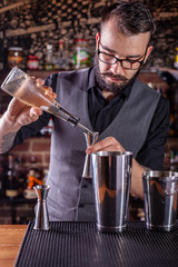 barman preparing cocktai and pours liquid into the jigger in a cocktail bar