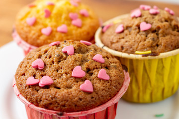 Delicious homemade colorful cupcakes with heart-shaped confectionery close up on a brown wooden background