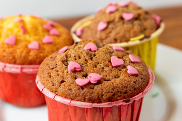 Delicious homemade colorful cupcakes with heart-shaped confectionery close up on a brown wooden background