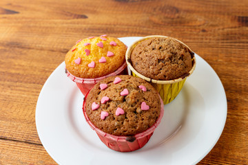Delicious homemade colorful cupcakes with heart-shaped confectionery close up on a brown wooden background