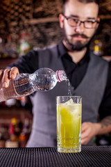 Bartender pouring a cocktail from the steel shaker on the bar counter on the blurred background