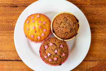 Delicious homemade colorful cupcakes with heart-shaped confectionery close up on a brown wooden background
