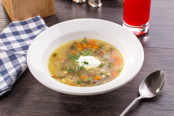 Soup Rassolnik with pickled cucumber and sour cream on wooden table