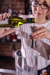 Female barman preparing cocktai and pours liquid into the jigger in a cocktail bar