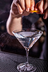 Male bartender squeezes a fresh orange rind in alcohol cocktail