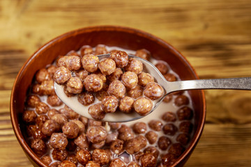 Cereal chocolate balls with milk in a bowl on wooden table. Spoon with breakfast
