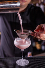 Bartender pouring a cocktail from the steel shaker on the bar counter on the blurred background