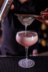 Bartender pouring a cocktail from the steel shaker on the bar counter on the blurred background