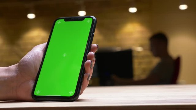 Closeup back view shoot of female hand playing a video on the phone with green chroma screen holding it vertically in the office indoors
